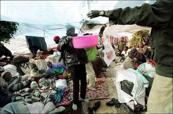 A Sudanese removes rainwater from a tarp in the protest camp, December 25, 2005. Five days later police attacked the camp. Photo by Shane Baldwin, New York Times